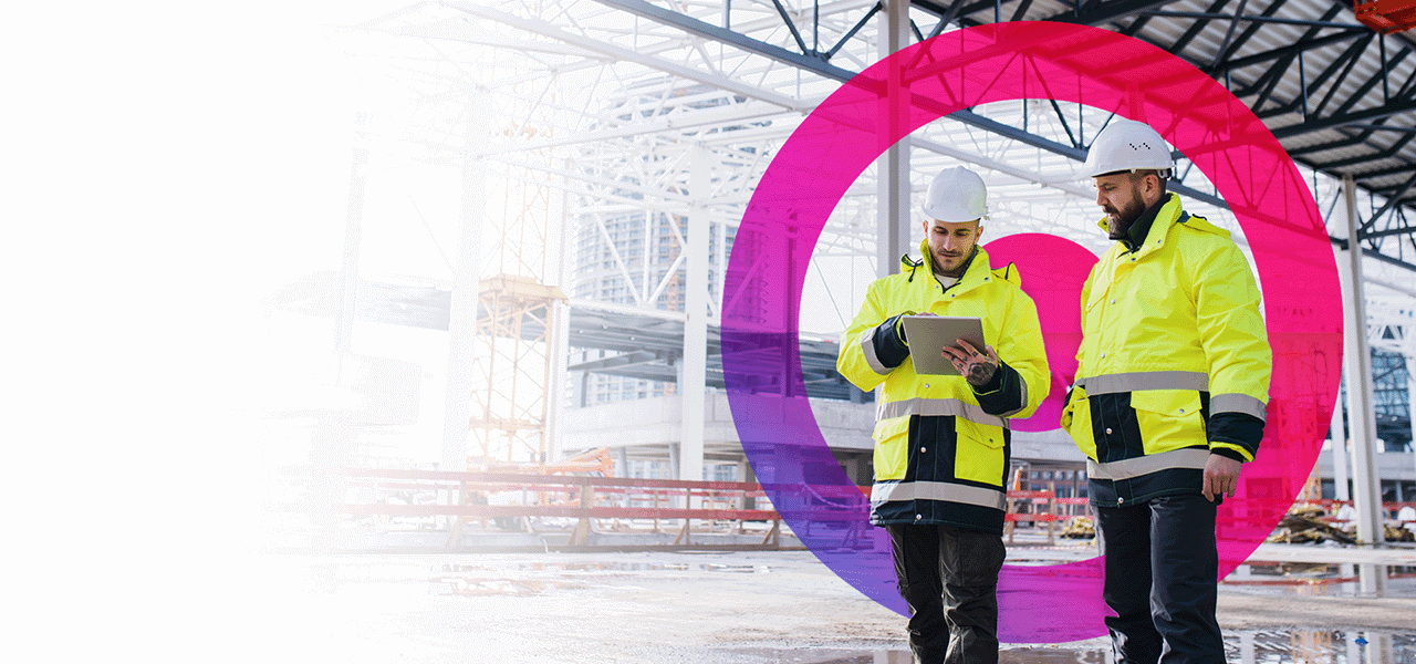 Two engineers on site wearing white hard heats and high visibility jackets. One man is using an iPad.