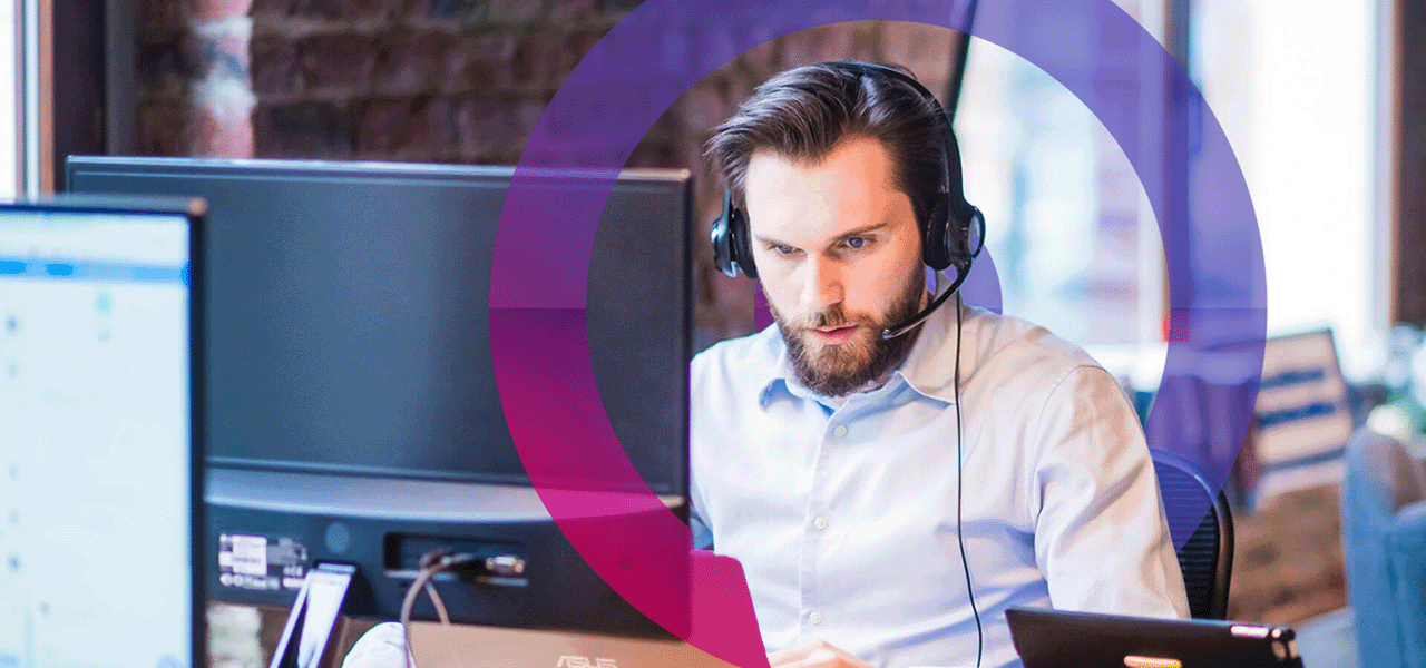 project security it support engineer working on a computer with a focused look. He is wearing a blue shirt and has a headset on him. Pink and blue cora lens in the background of photo