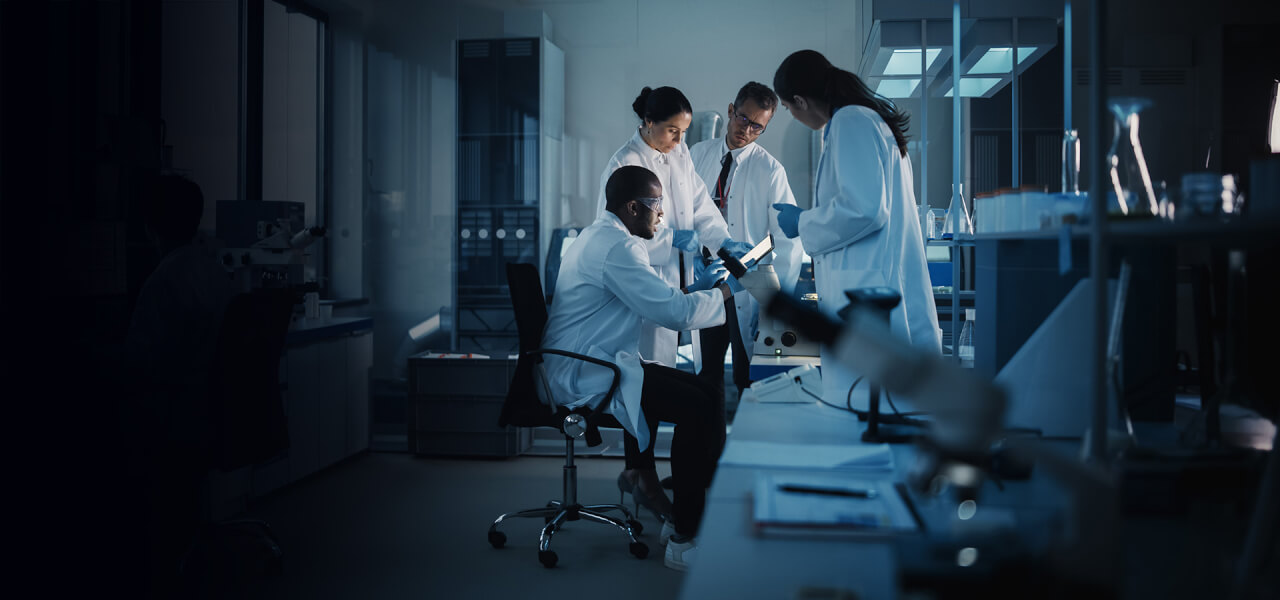 a team of 4 scientists wearing white lab coats analysing the results of an experiment in a large lab.