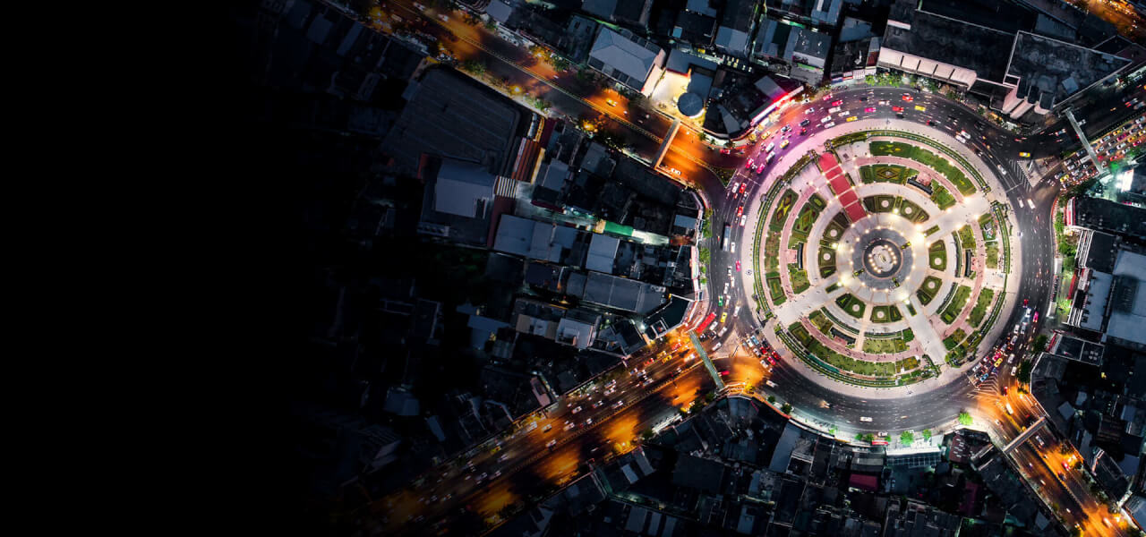 An aerial photo of a city at night with lots of large buildings and a bright roundabout with cars driving