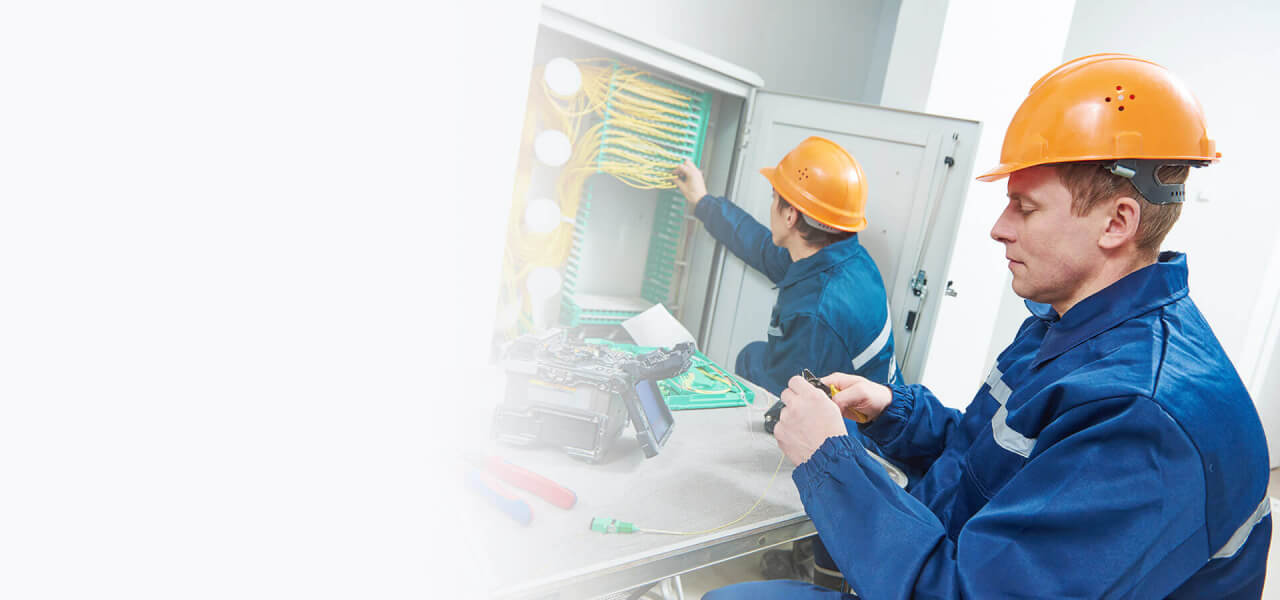 two male telecom engineers wearing yellow hard hats and blue all in ones fixing wires.