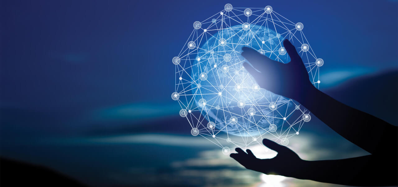 An image of shadowed hands holding a lit up globe of the world with interconnected lines going across it.
