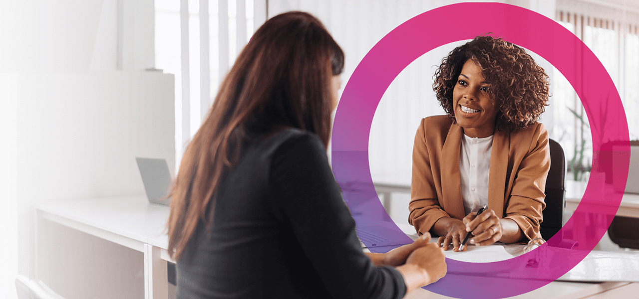 2 women in an office talking through finances. pink and purple Cora lens to right side of photo