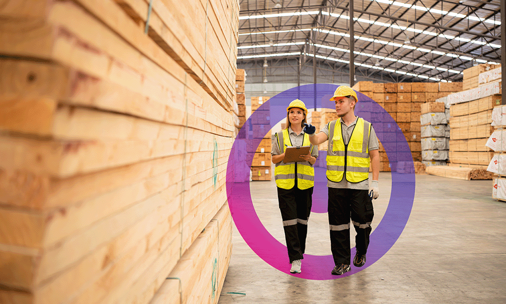 Man and woman wearing yelllow high vis and hard hats on manufacturing floor having a discussion