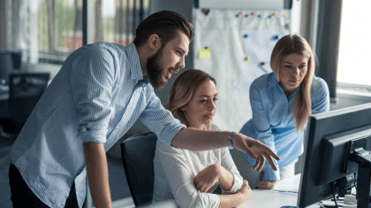 1 man and 2 women working together on a project looking at a computer in an office environment