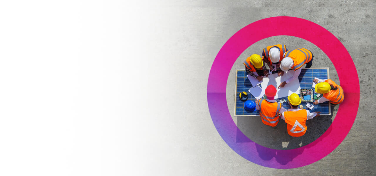 A group of engineers wearing orange high vis coats looking at plans for a project on a large sheet of paper. A pink cora lens is circling the group.