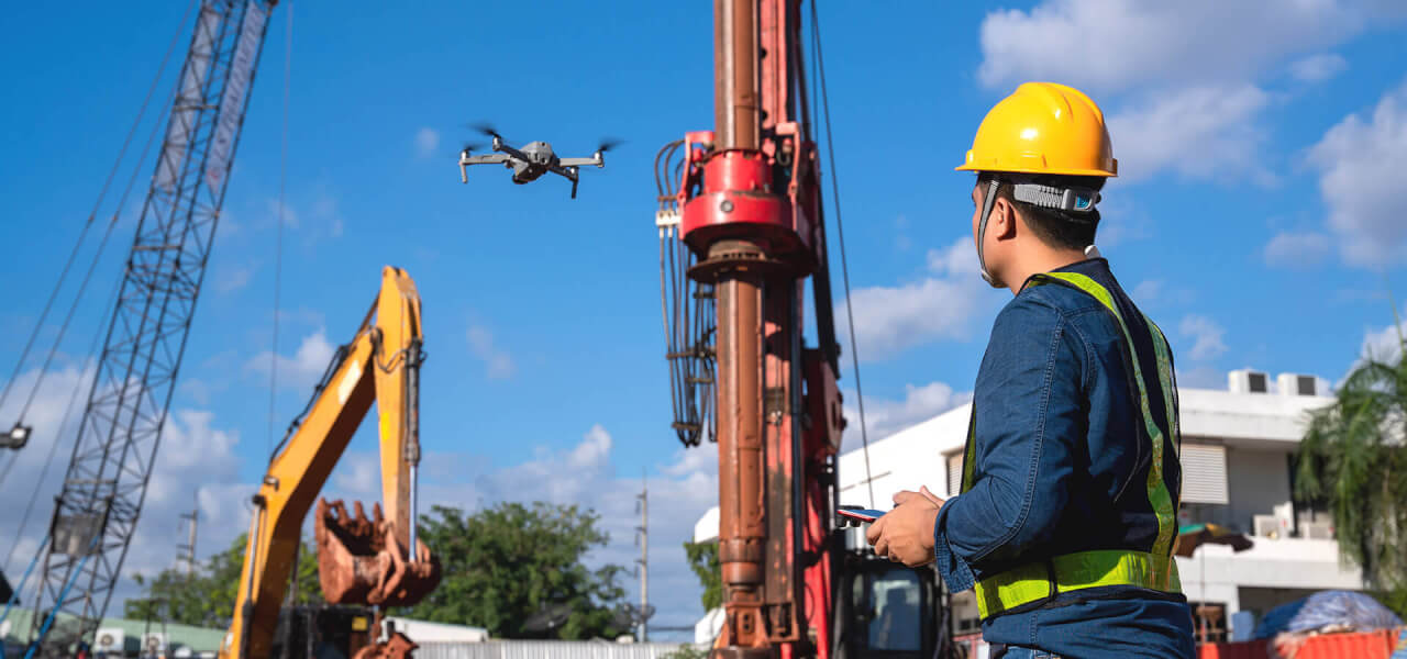 Man wearing a yellow hard hat that is controlling a drone on a construction site