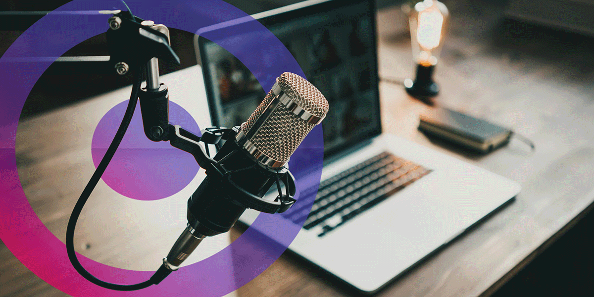 Podcast set up with microphone and laptop in a studio. pink and blue cora lens logo on left of picture behind the microphone.