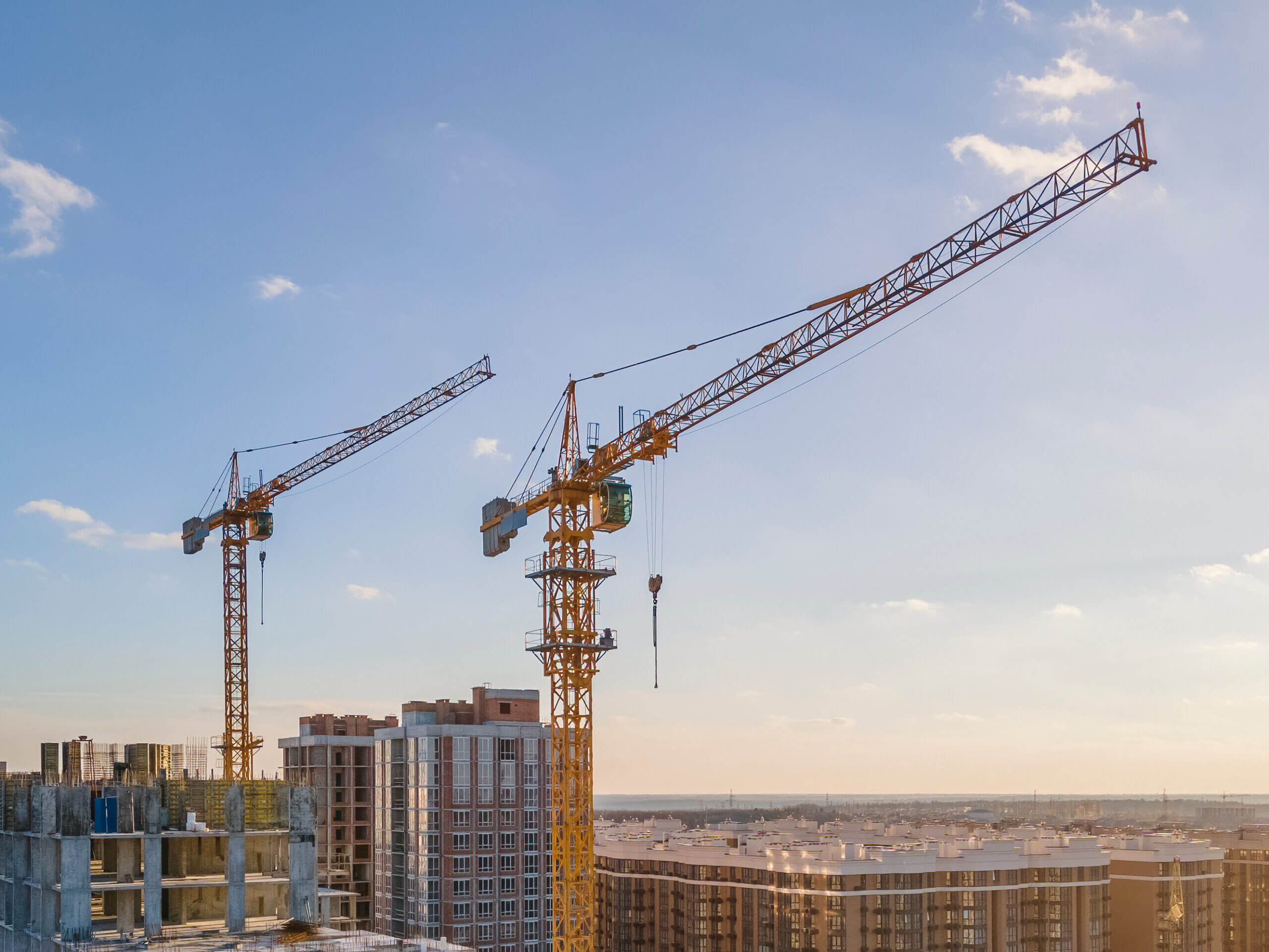 Cranes on the construction site surrounded by new real estates. Scenic aerial photo of growing city districts