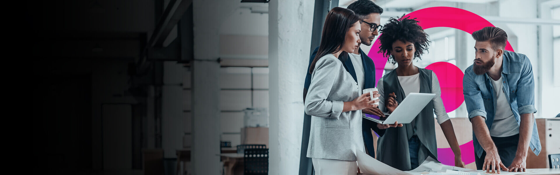 Team of two men and two women working in an office standing at a desk discussing work. Cora systems pink and purple logo lens in the background.