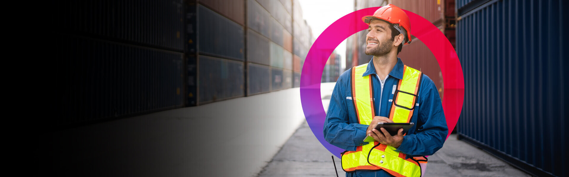 Supply Chain Management 1920x600 Man in an orange hard hat and a yellow high visibility jacket with an iPad taking notes walking through a container warehouse,