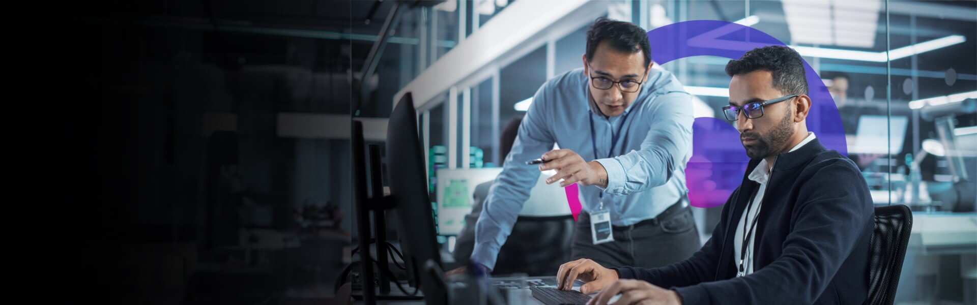 Two men discussing work in an office. One is pointing at a computer while talking.