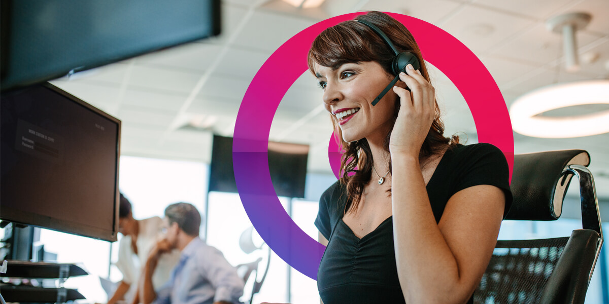 Woman with brown hair wearing a headset and mic holding her hand up to her ear listening to the caller.
