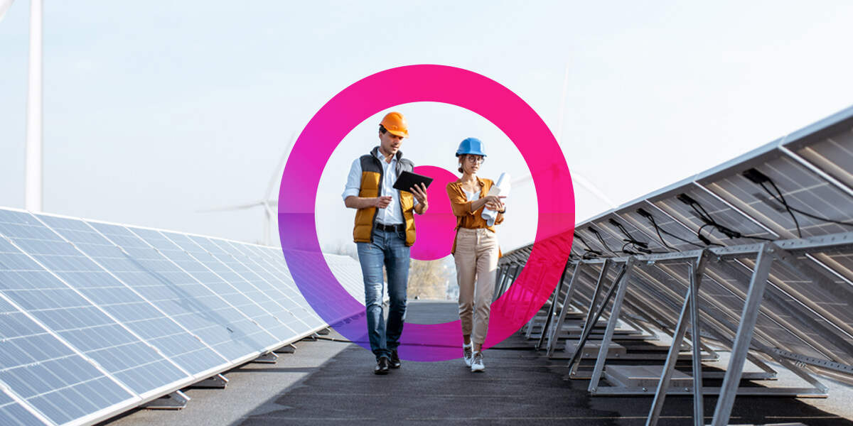 Two people walking on solar panel farm wearing hard helmets and high visibility jackets. Pink and purple lens graphic in the background.