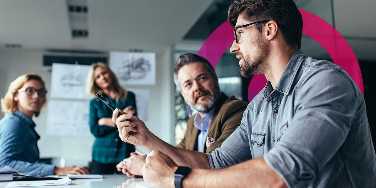 A team of two men and two women having a meeting. On man has a beard and brown hair with glasses wearing a blue shirt and is pointing his finger. Pink and purple lens in the background.