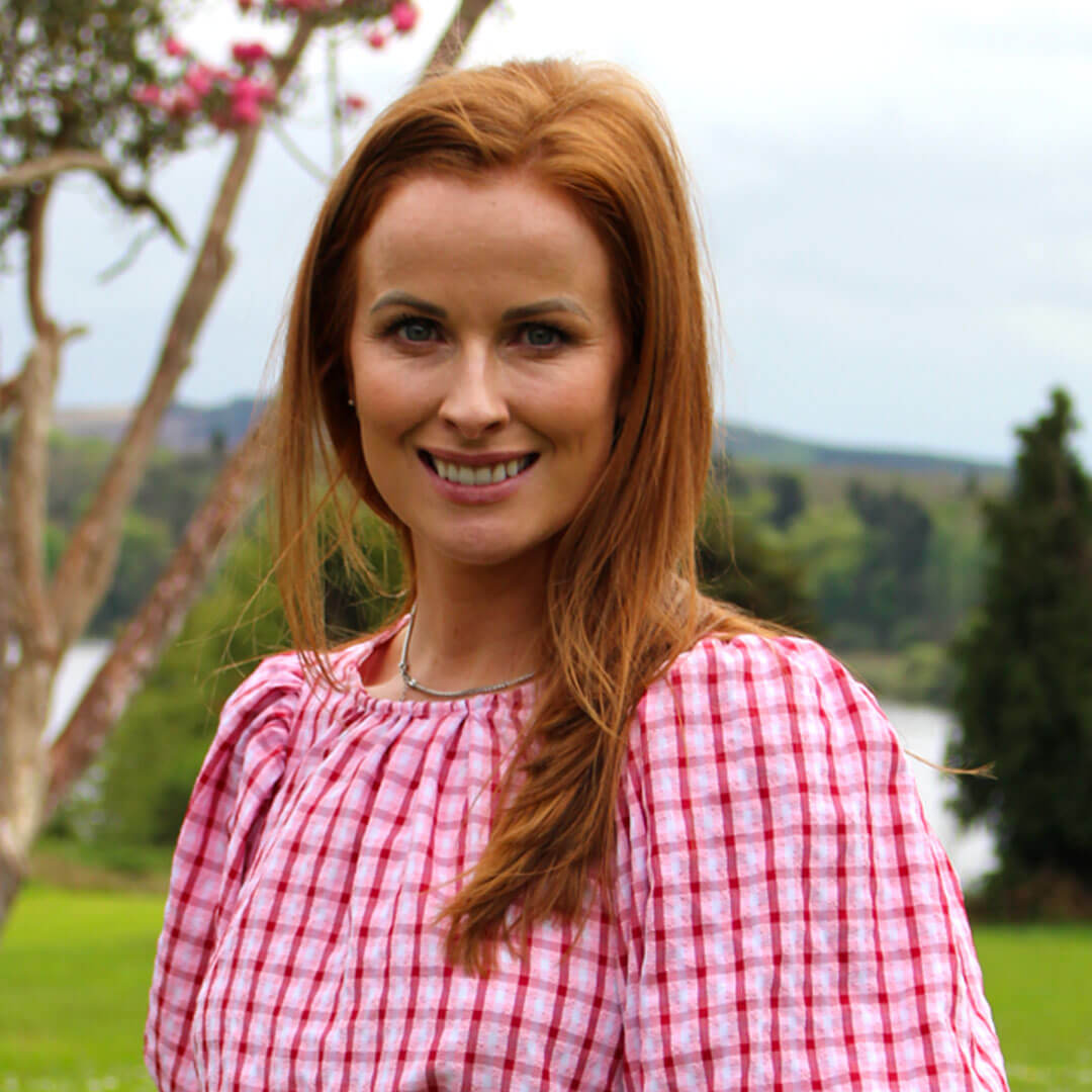 Woman with red hair smiling wearing a white and pink top.