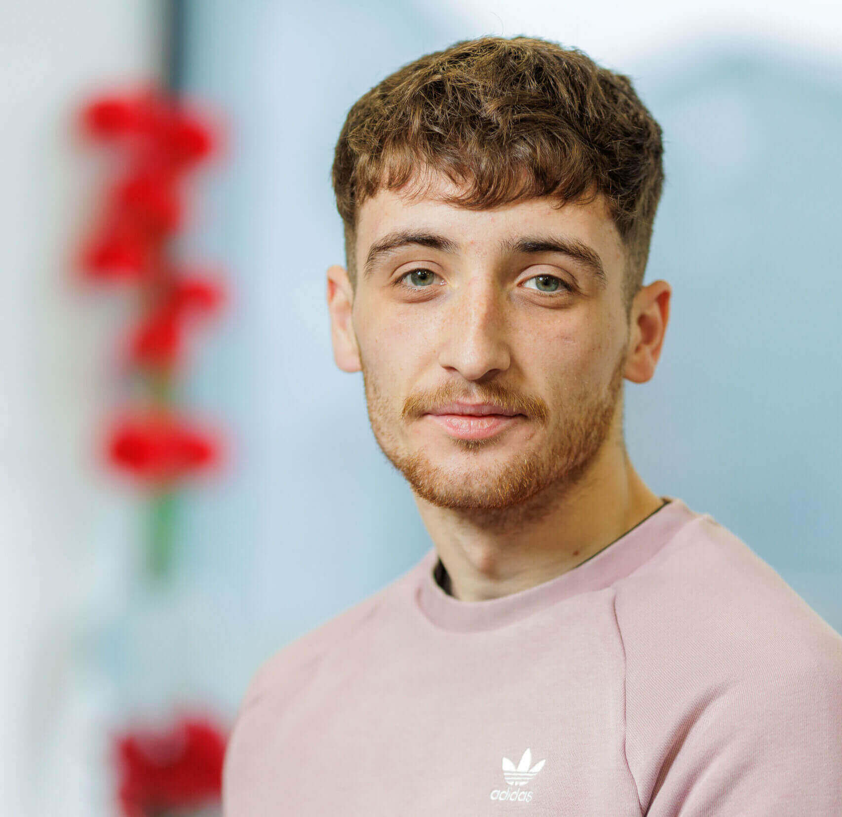 Man with brown hair wearing a pink adidas jumper